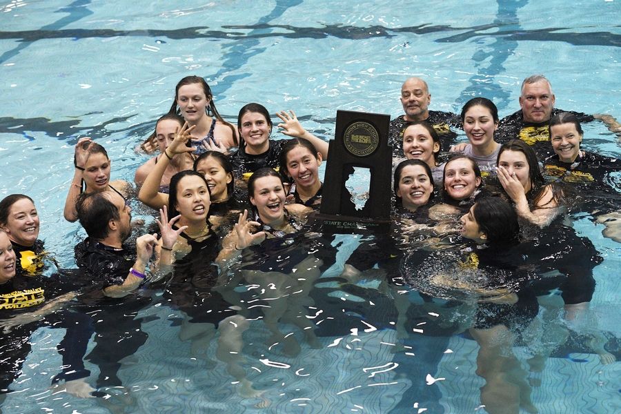 The team posing with their  state champions trophy and coaches in the pool