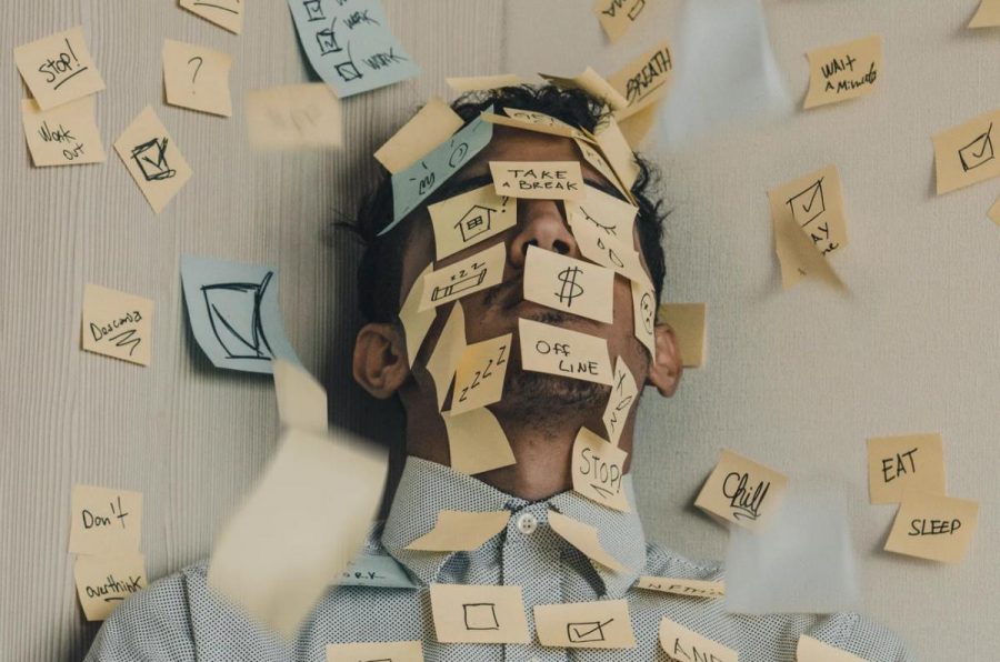 A man lays down on the floor, with a flock of sticky notes with reminders surrounding him.